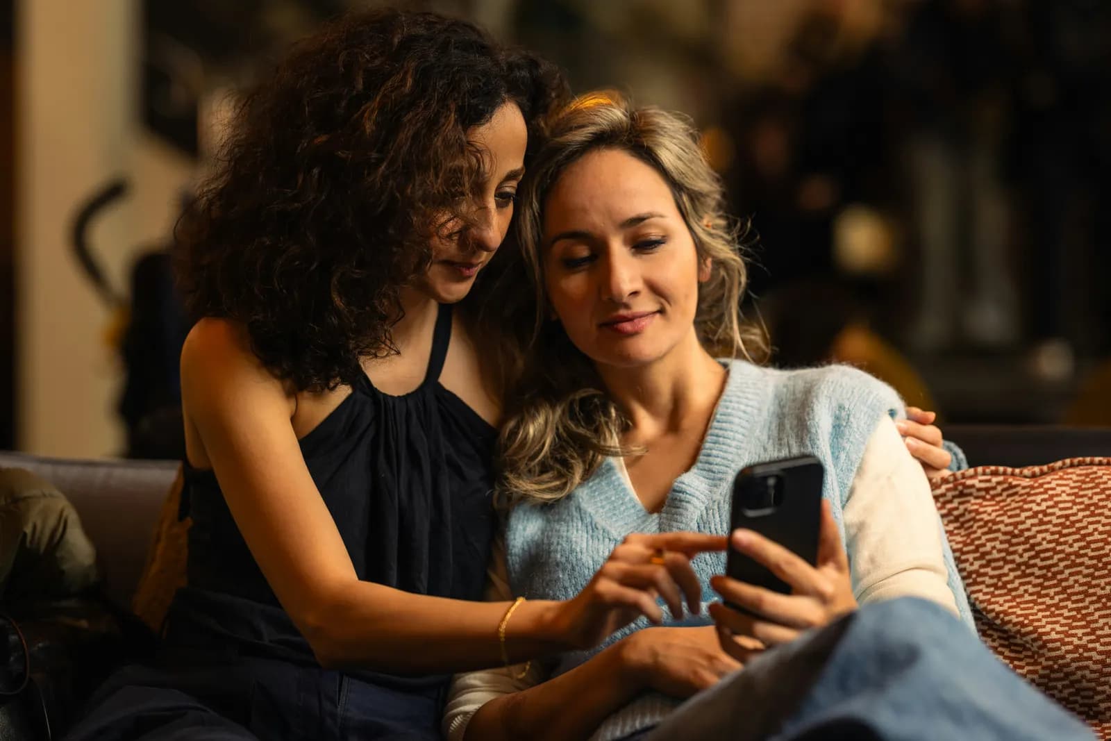 Two women sit on a sofa and look at a phone together
